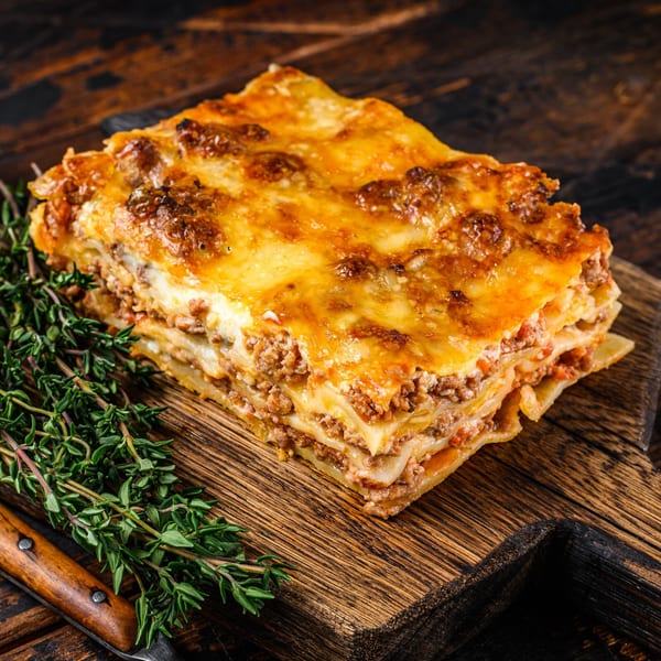 A golden-brown baked lasagna with layers of pasta, meat, and cheese, garnished with fresh thyme.