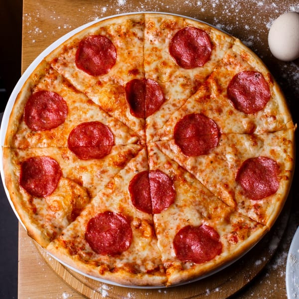 A whole pepperoni pizza, sliced into eight pieces, on a wooden board dusted with flour.