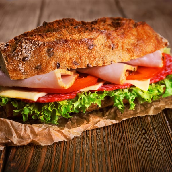 A large, crusty baguette sandwich filled with deli meats, cheese, lettuce, and tomatoes on a wooden table.