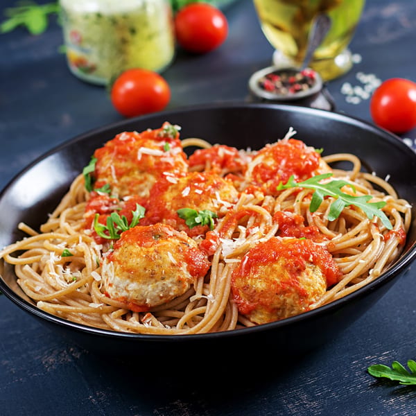 Spaghetti with meatballs, tomato sauce, parmesan, and arugula in a black bowl.